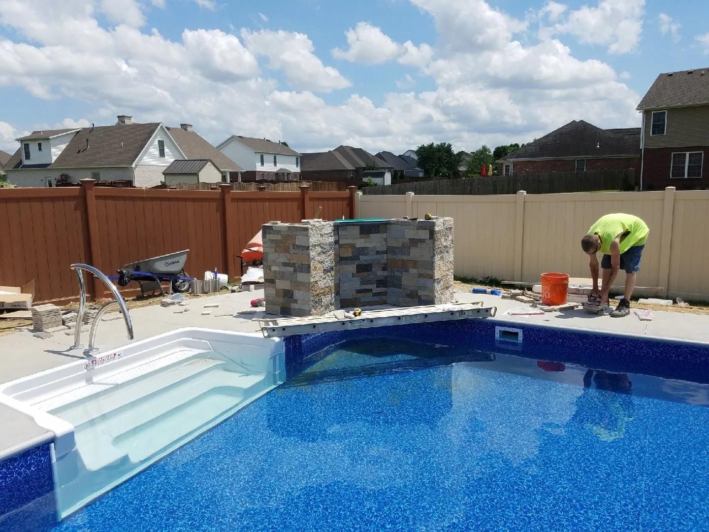 A man in a yellow vest is working on a swimming pool.