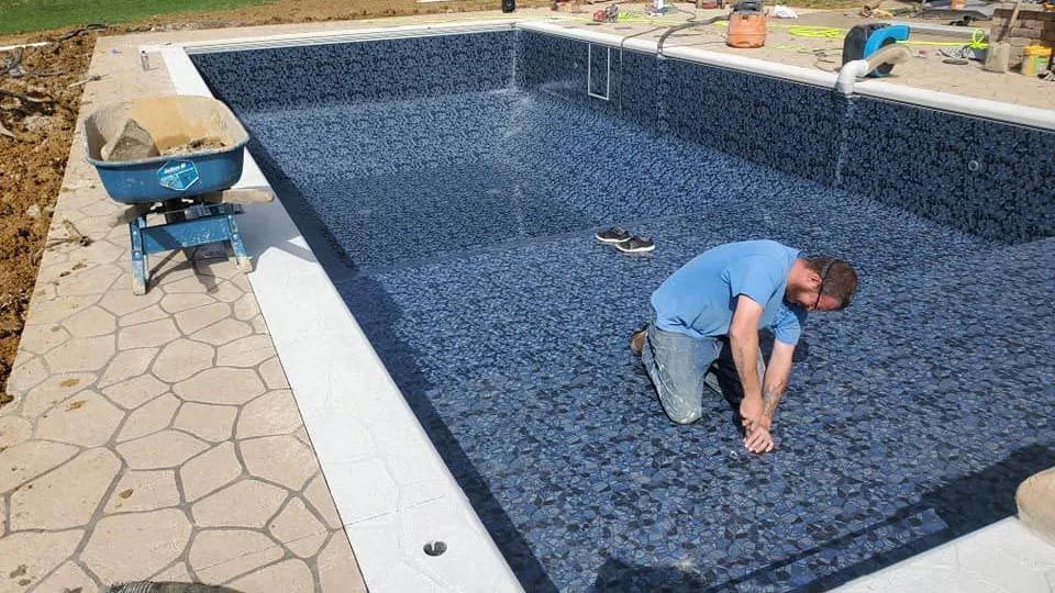 A man is kneeling in front of a swimming pool.
