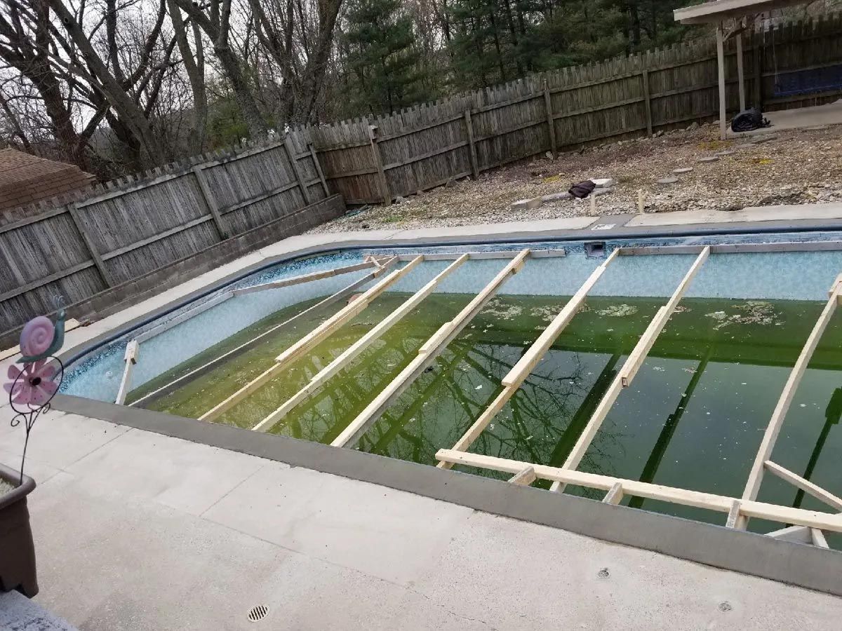 An empty swimming pool with a wooden fence in the background.