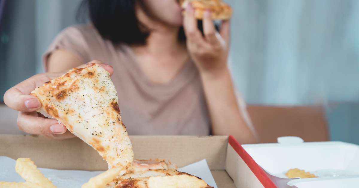 A young woman binge eating pizza while reaching for more