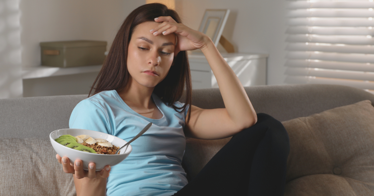 Young woman in a blue shirt looking at a bowl of food with distress