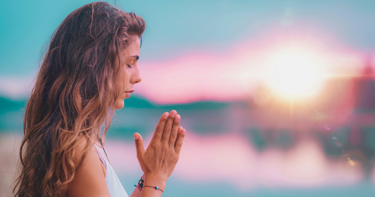 Woman meditating against a colorful sunrise