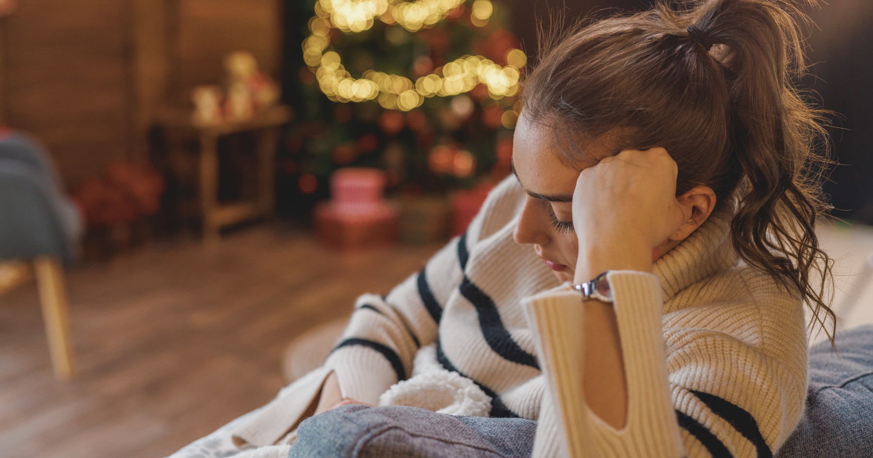 sad woman sitting in a room decorated for the holidays, looking down at her lap