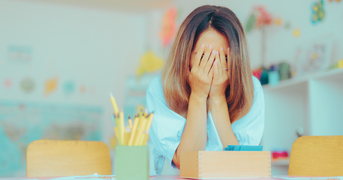 Teacher with her head in her hands, appearing overwhelmed in the classroom.
