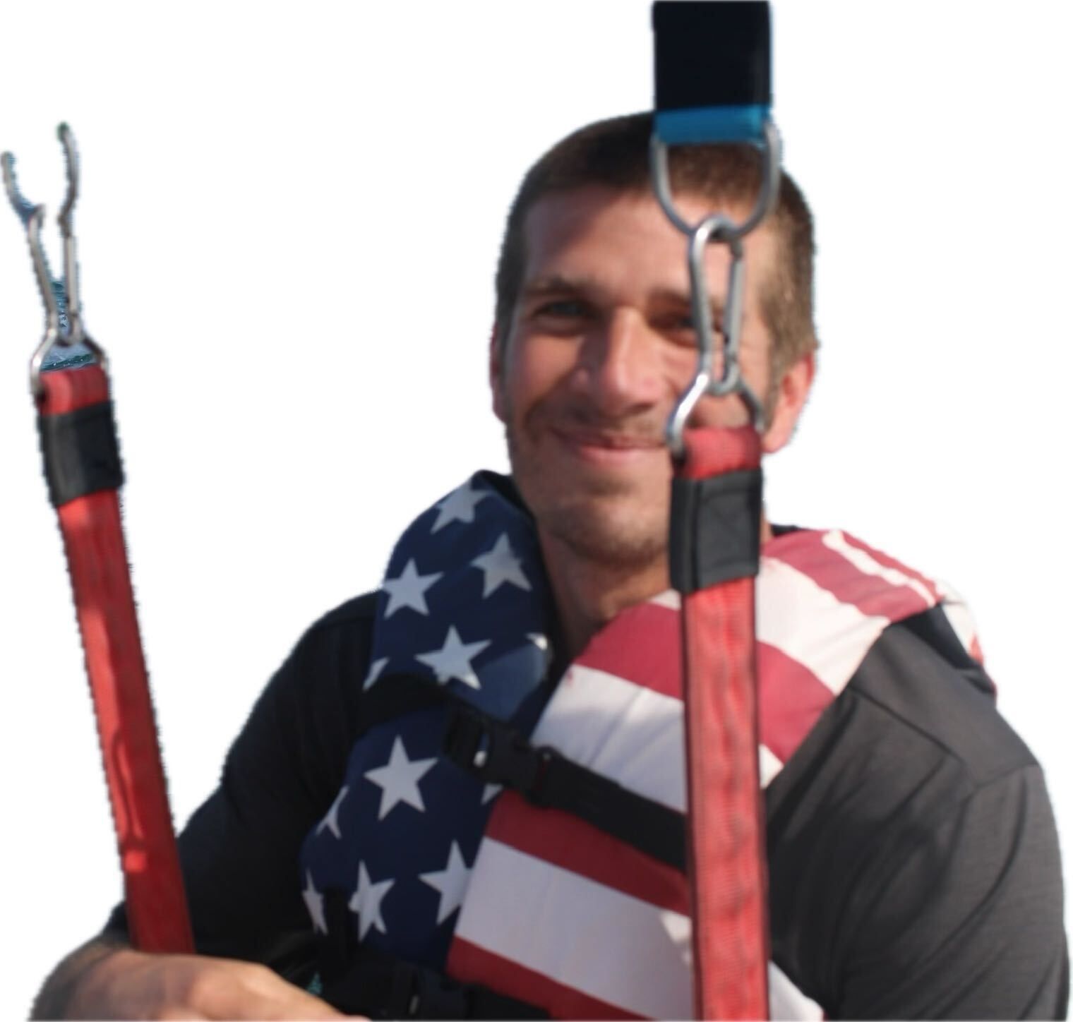 Man in life vest with American flag design, holding red straps with hooks. Smiling.