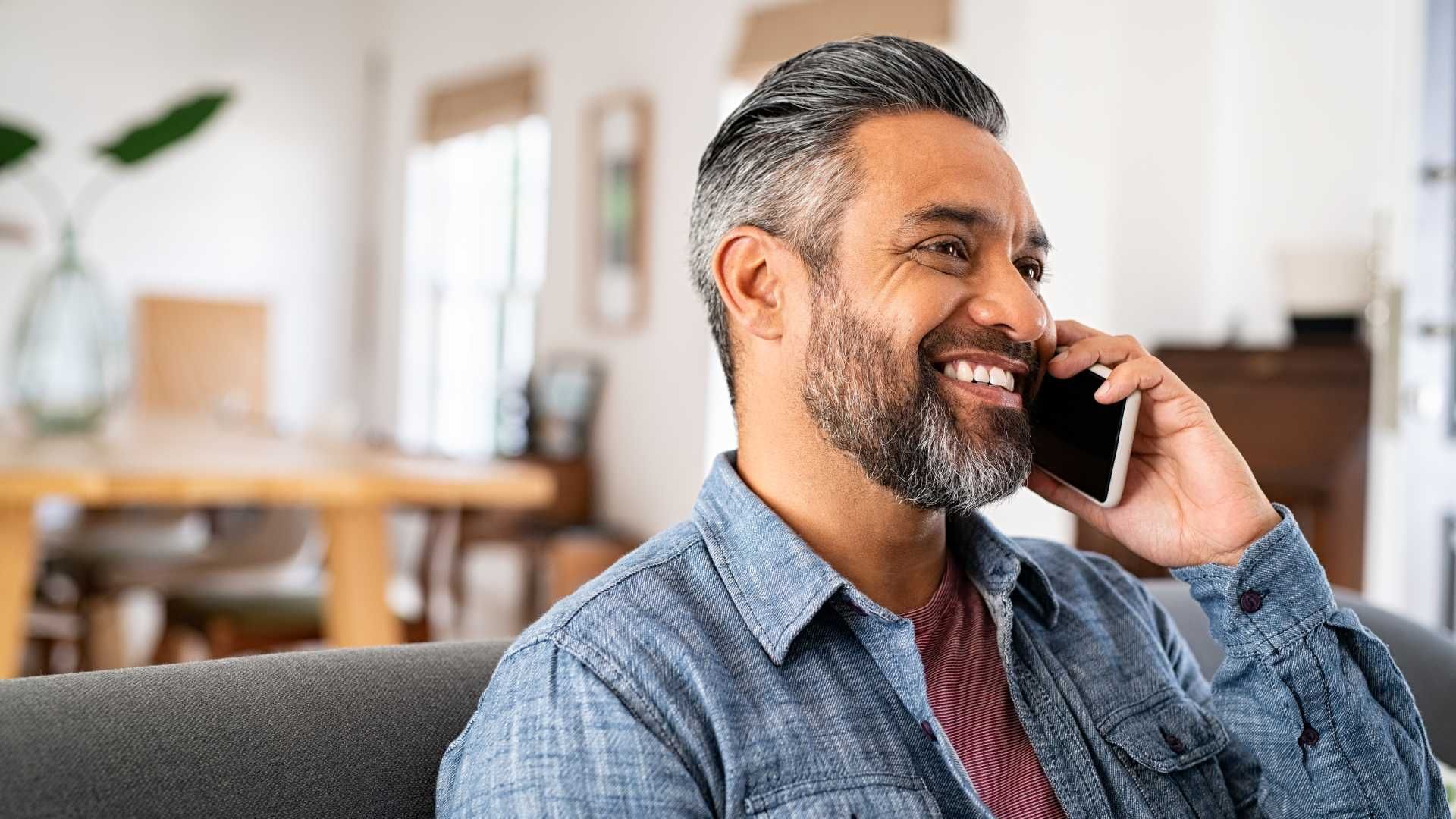 A man is sitting on a couch talking on a cell phone.