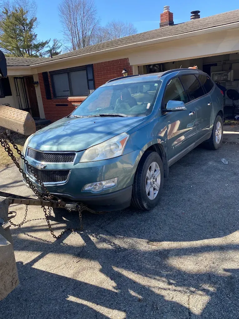 A blue suv is parked in front of a house with a trailer attached to it.