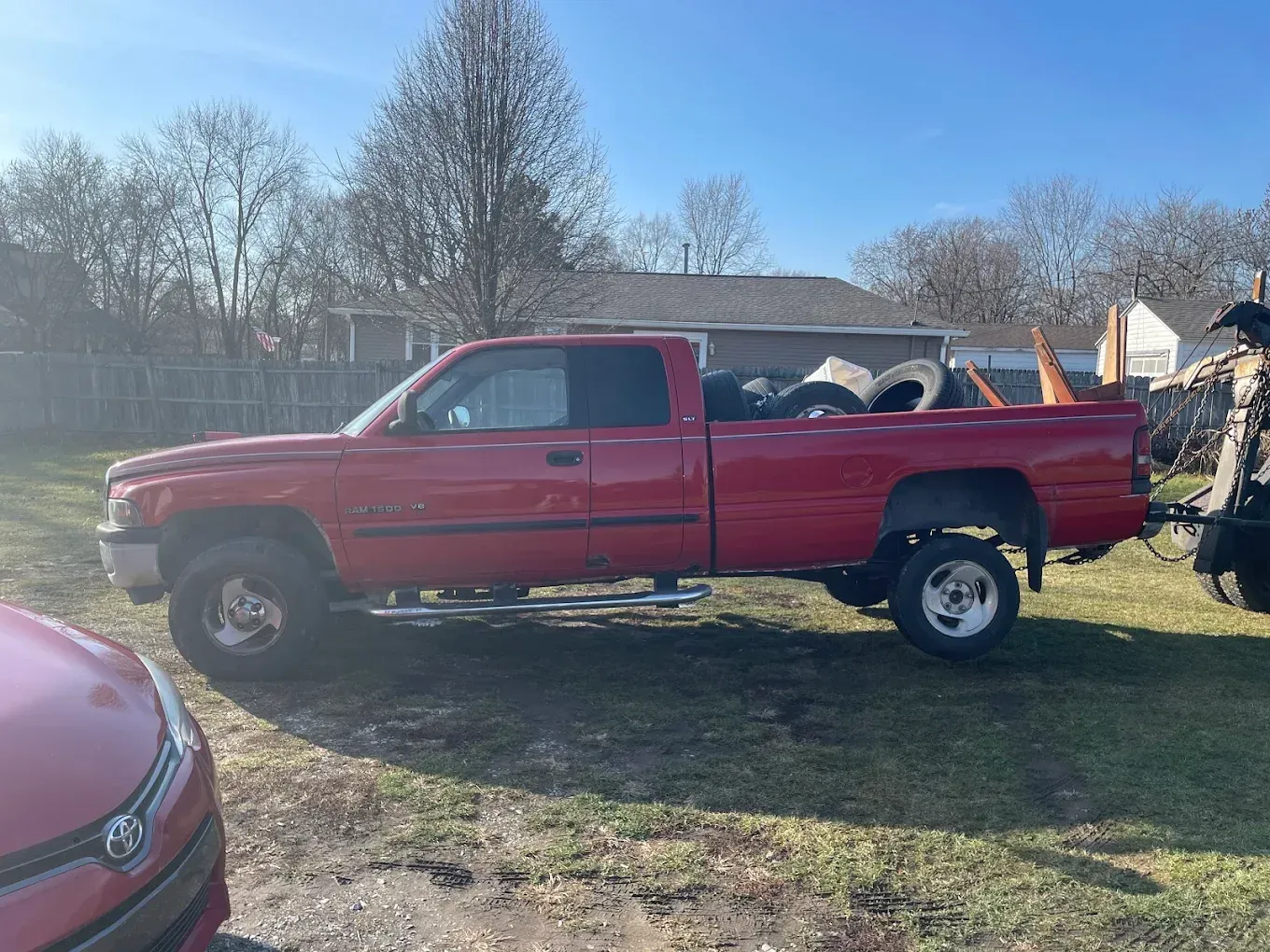 A red truck is parked in a grassy field next to a red car.