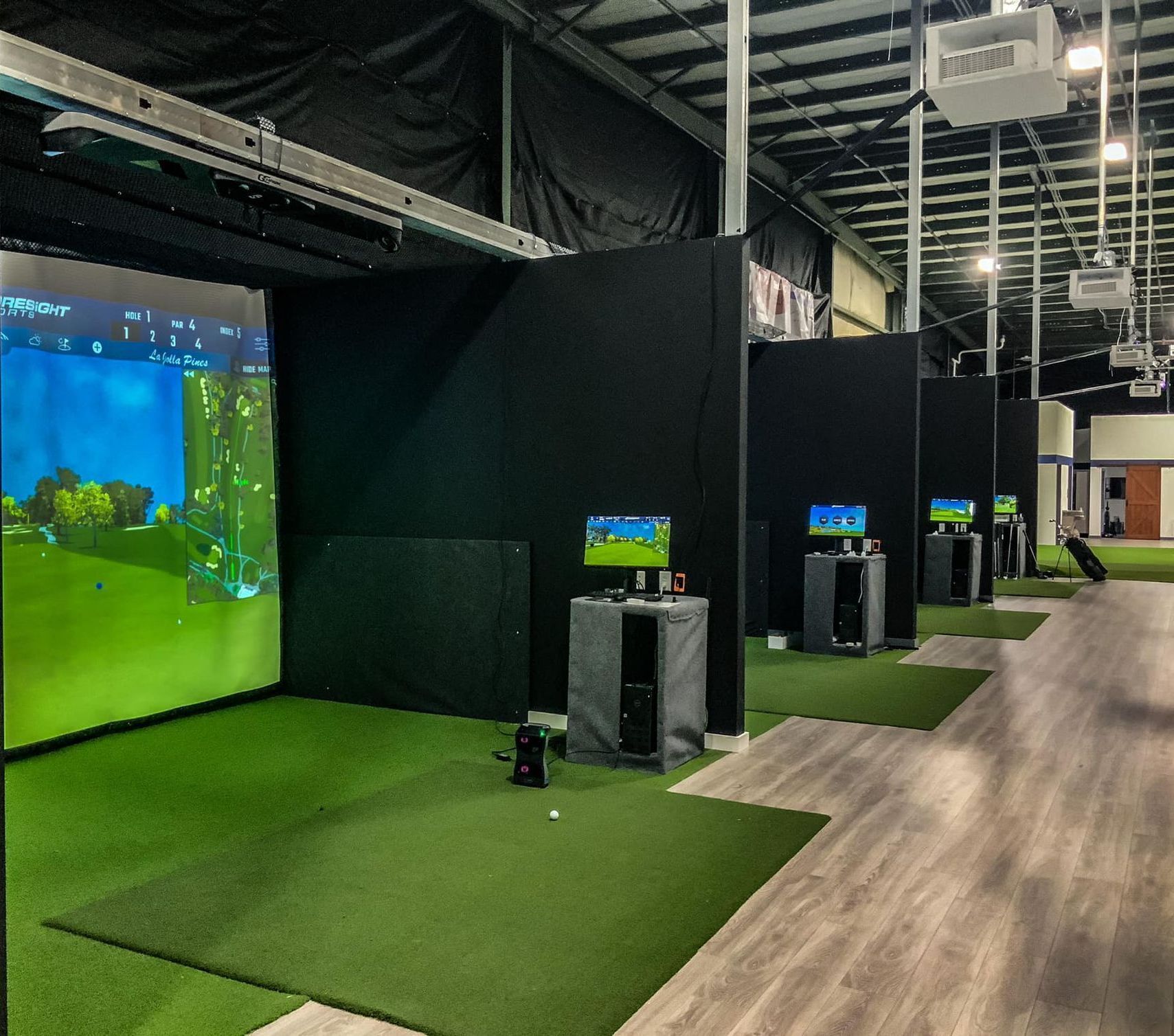 A row of golf simulators are lined up in a warehouse.
