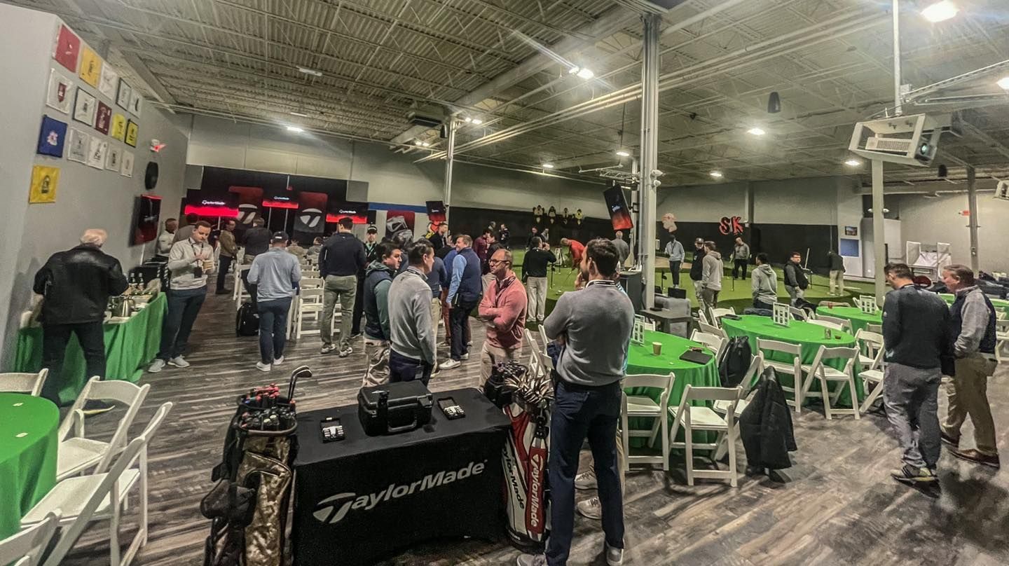 A group of people are standing around tables and chairs in a large room.