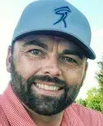 A man with a beard is wearing a baseball cap and smiling.