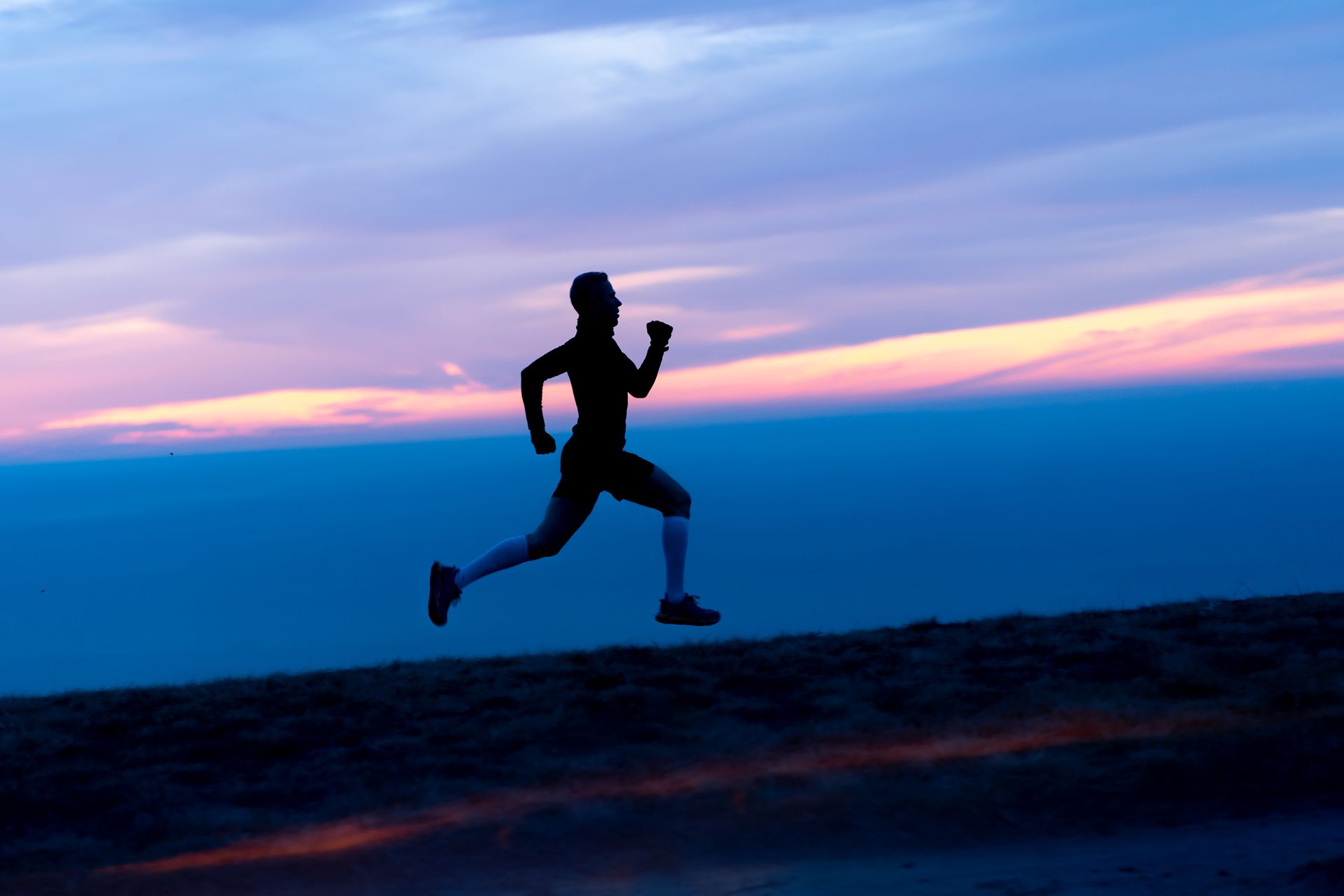 Silhouette of a person running uphill at dusk; sky with pink and blue hues.