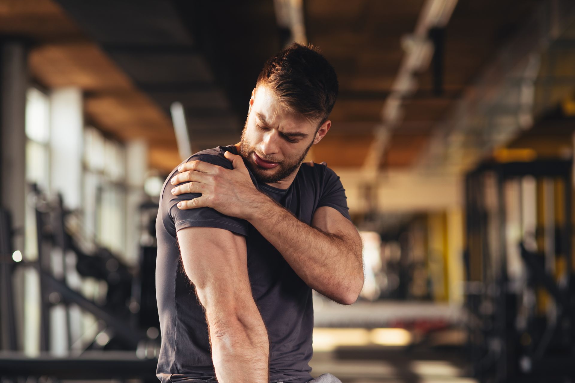 A man is holding his shoulder in pain in a gym.