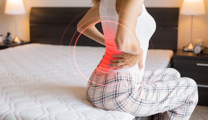 A woman is sitting on a bed with back pain.