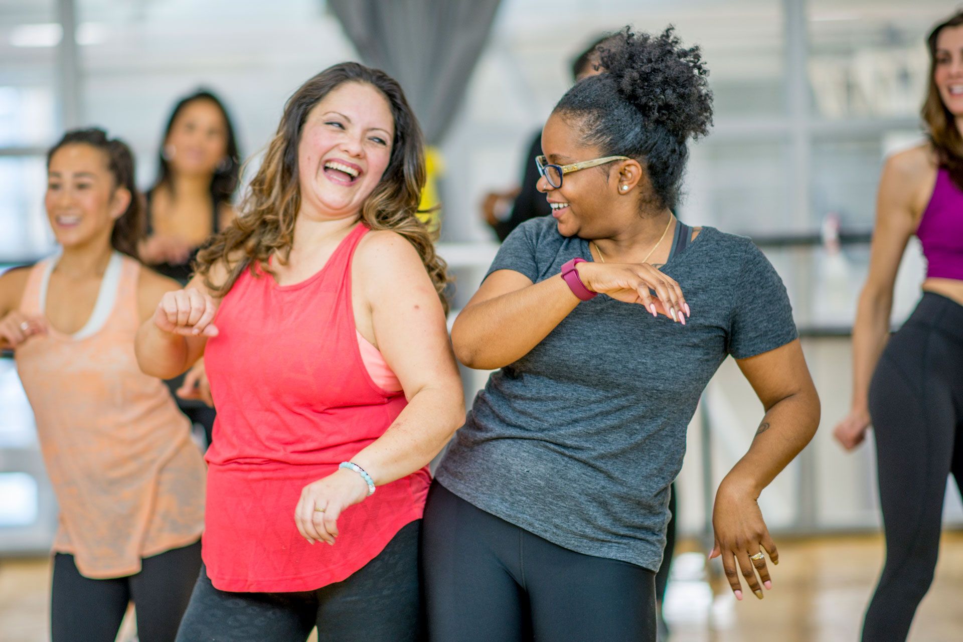 Group fitness class with participants dancing in a studio wearing athletic clothing.