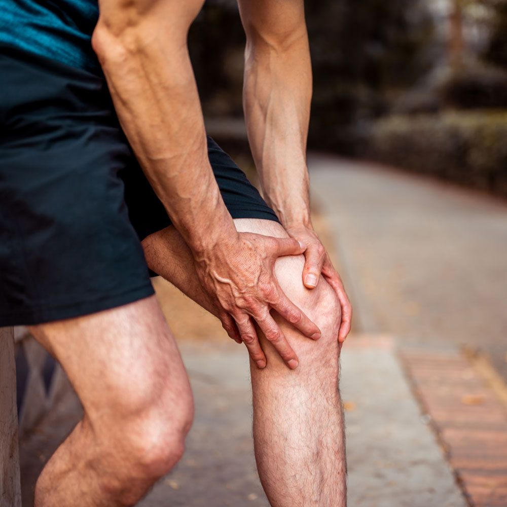 A man is holding his knee in pain while standing on a sidewalk.
