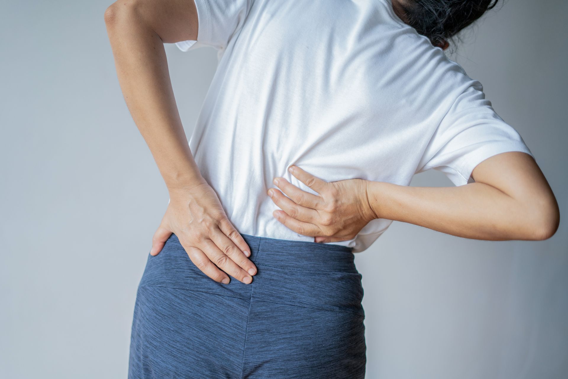 A woman massaging her back muscles due to intense low back pain. A woman massaging her back muscles due to intense low back pain.