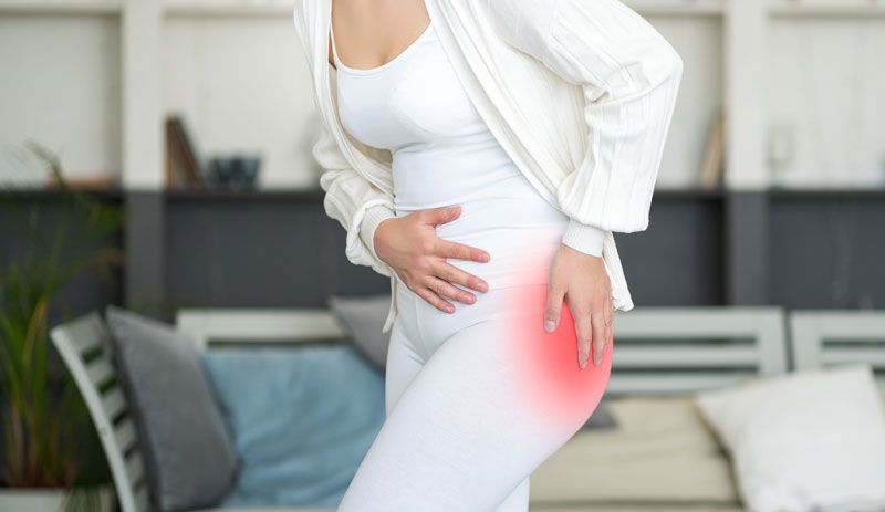 A woman is holding her hip in pain in a living room.