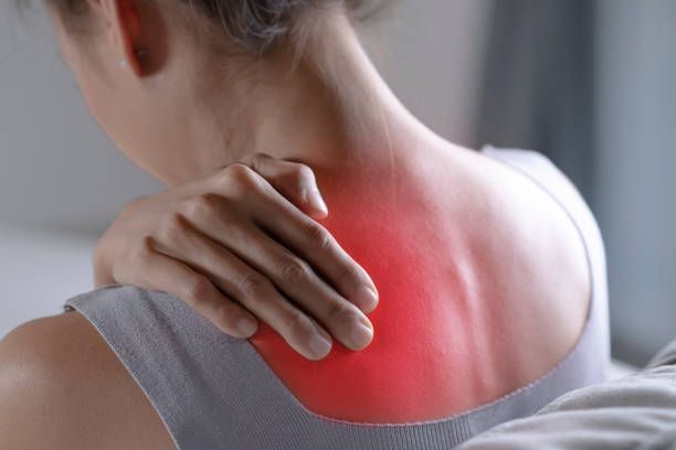 A woman is holding her neck in pain with a red spot on her back.