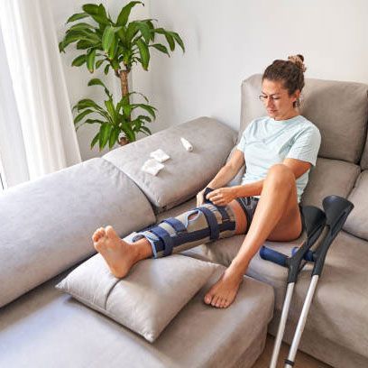 A woman with a knee brace is sitting on a couch with crutches.