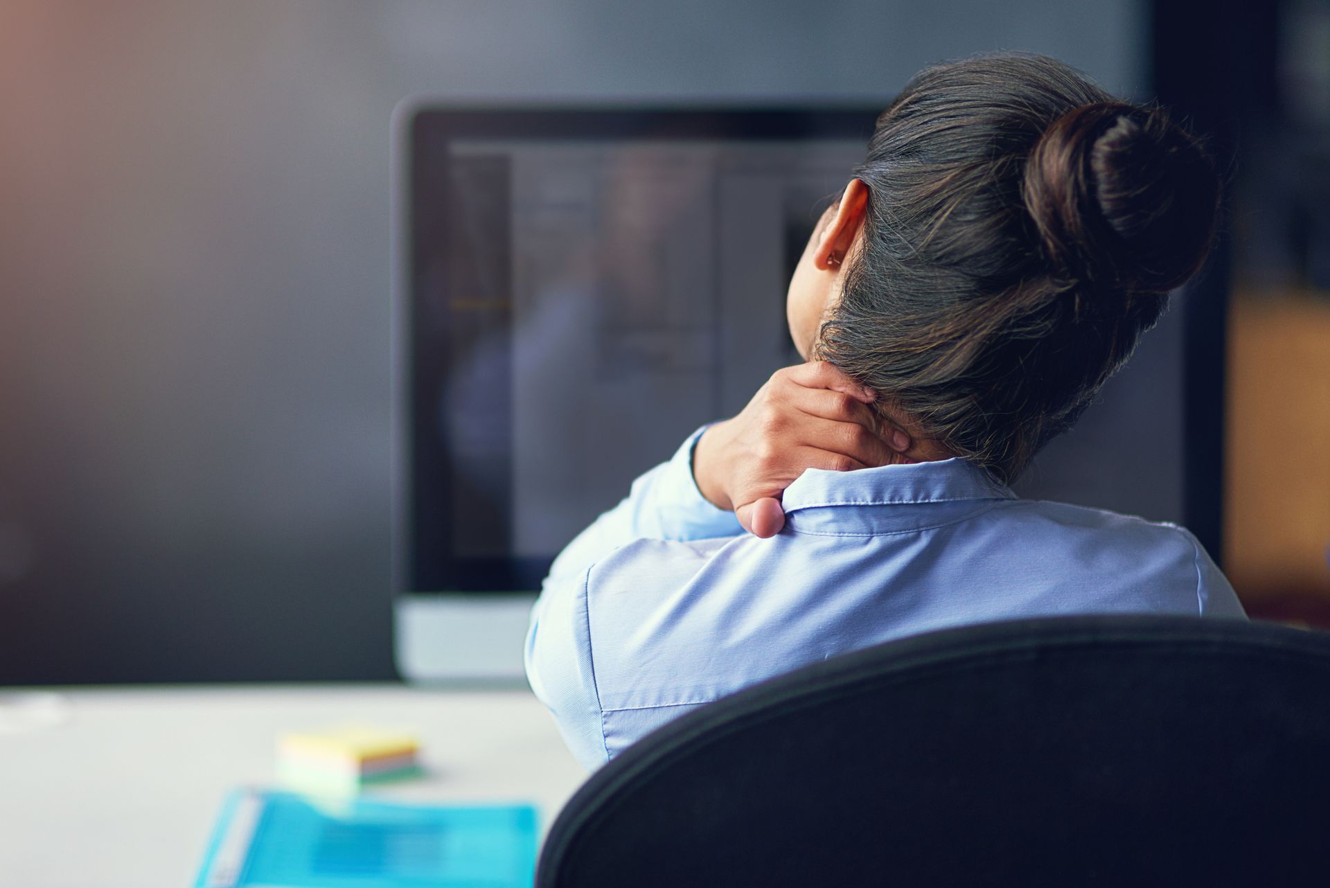 A woman is sitting in front of a computer holding her neck.