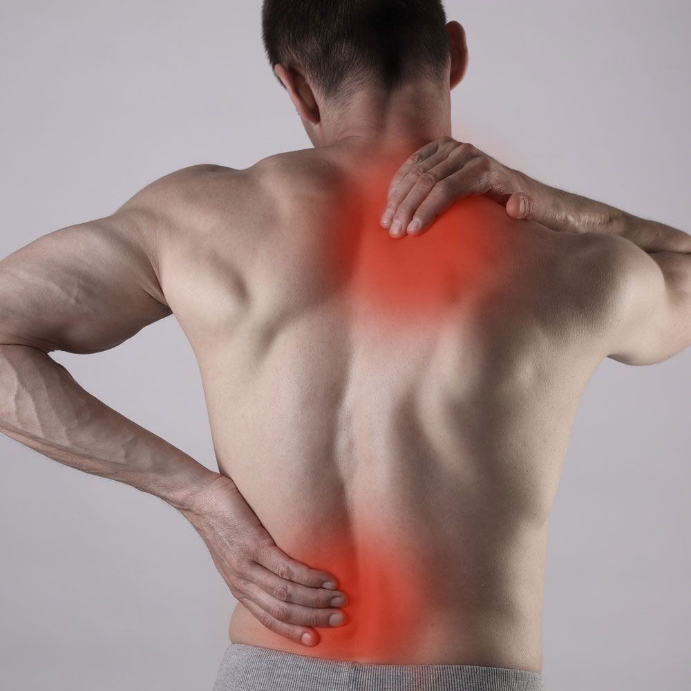 A shirtless man is holding his neck and back in pain