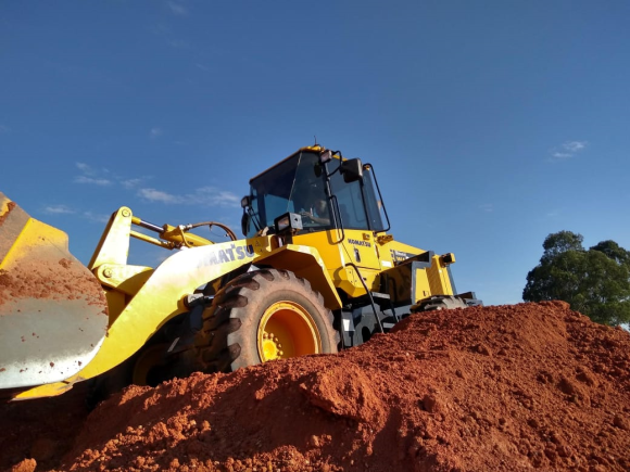 Uma escavadeira amarela está em cima de uma pilha de terra.