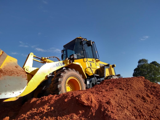 Uma escavadeira amarela está em cima de uma pilha de terra.