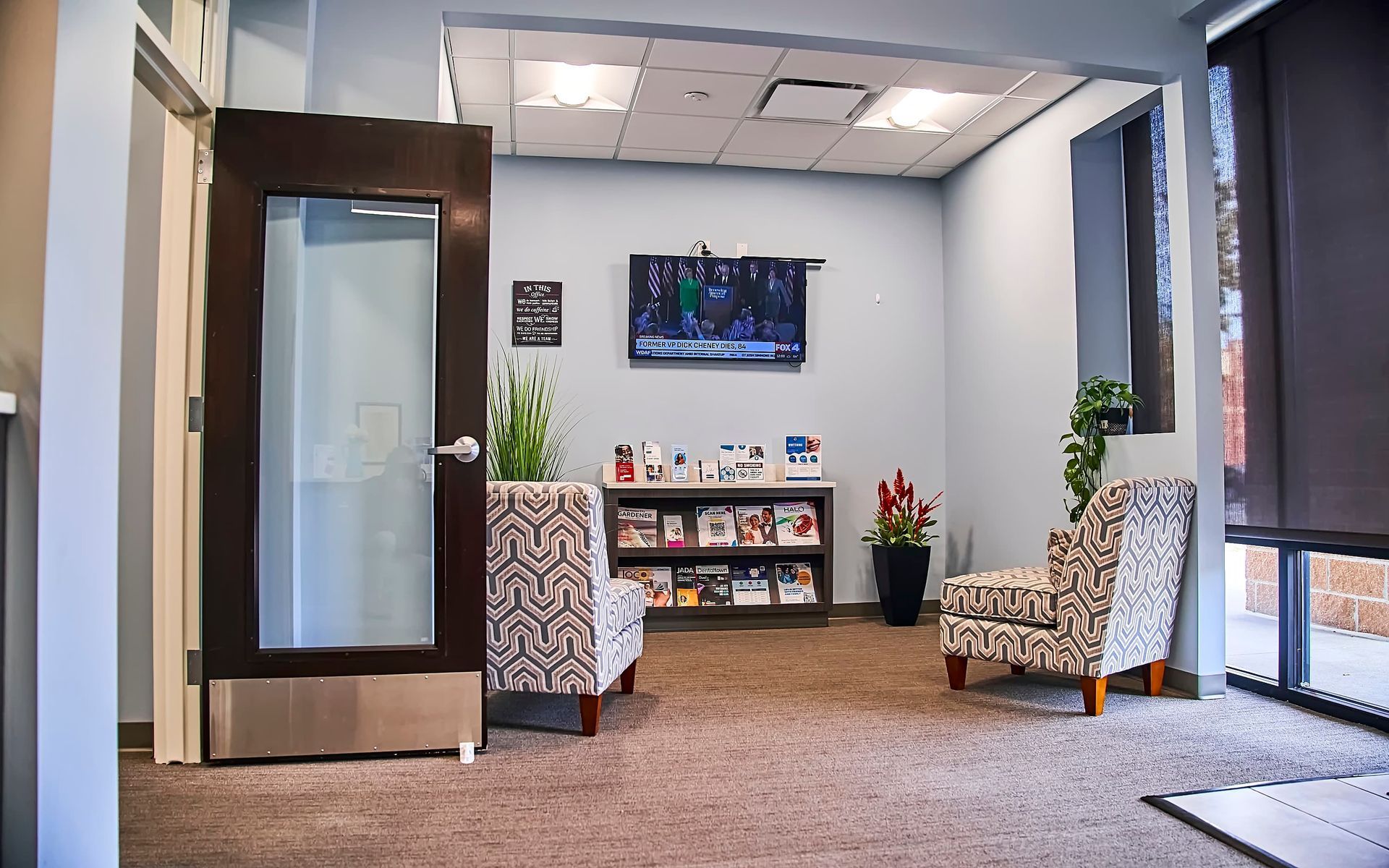 Waiting area with chairs, TV, bookcase, and a window.