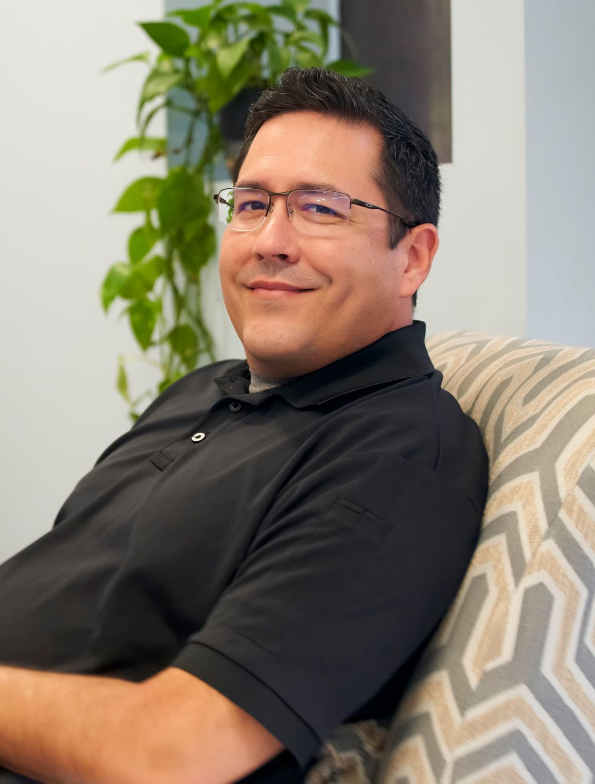 Man in gray scrubs smiles at the camera, inside a room with light-colored walls.