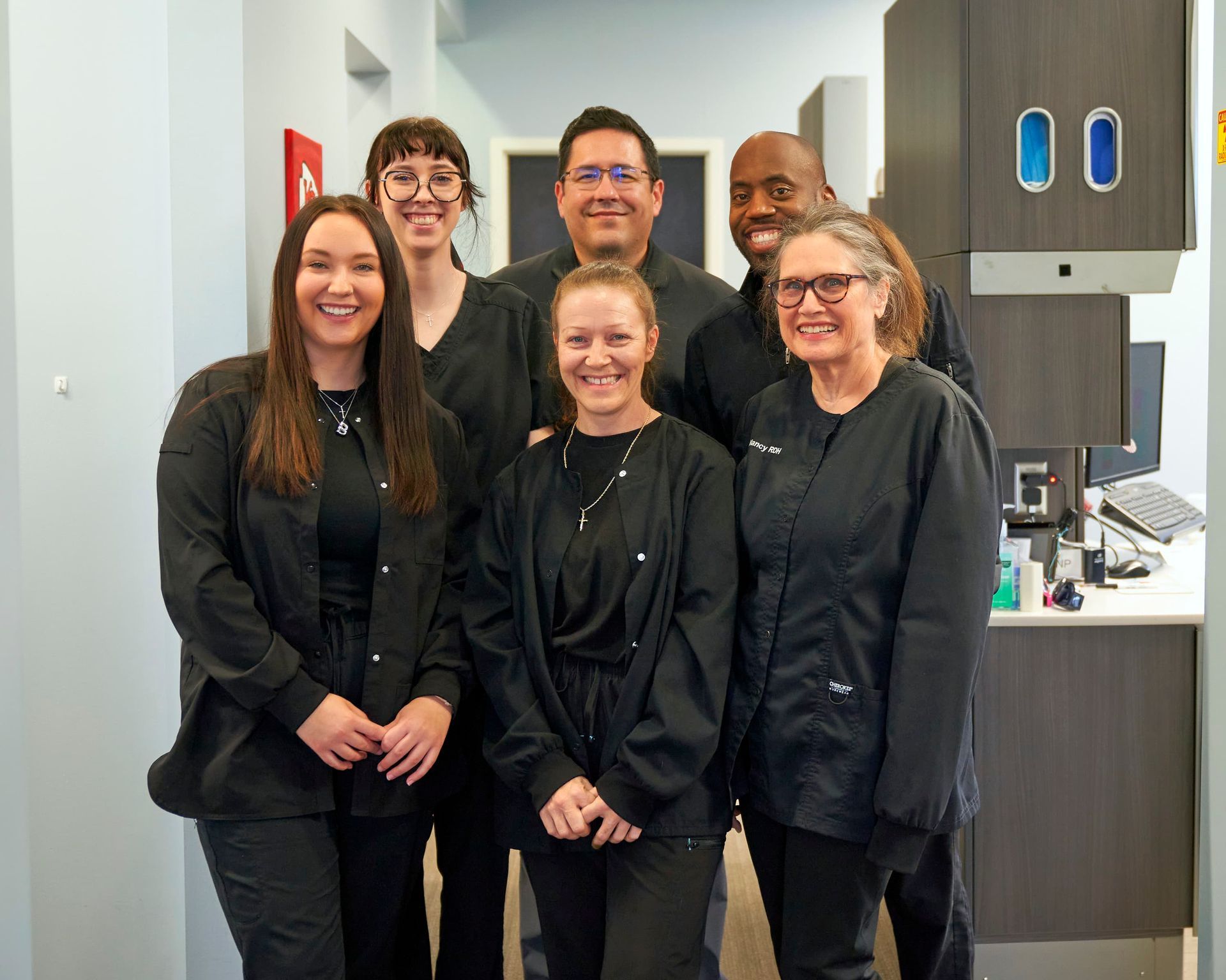 Three people smiling, posed outside brick building in blue uniform scrubs.
