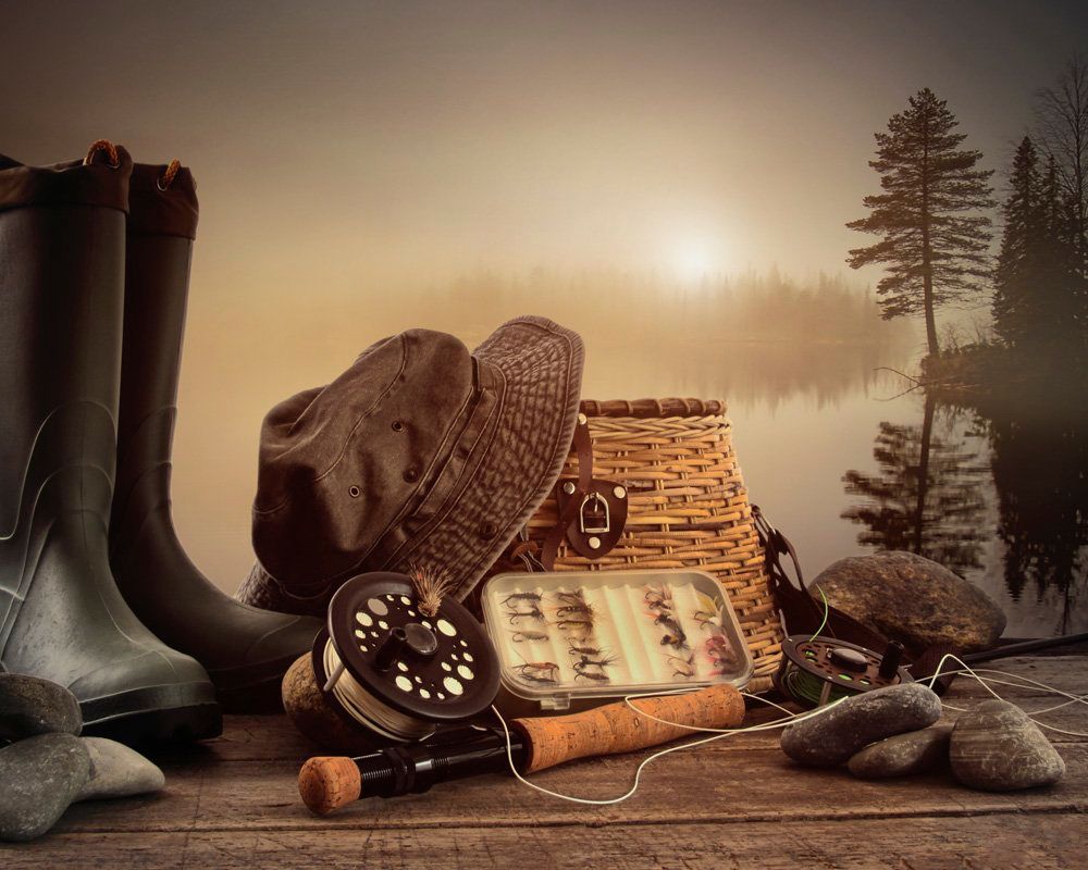 A fishing rod , hat , boots , and a basket are on a wooden table.