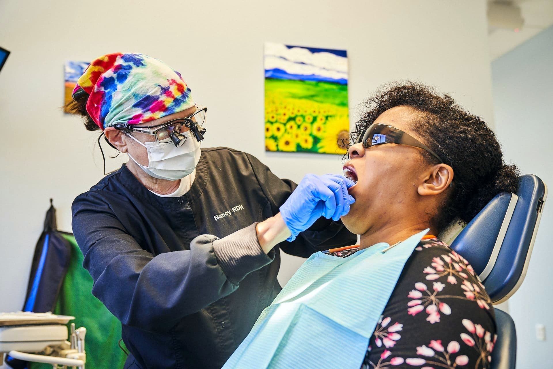 Dentist examining patient's teeth. Dentist wearing mask, gloves, and glasses. Patient has mouth open in dental chair.