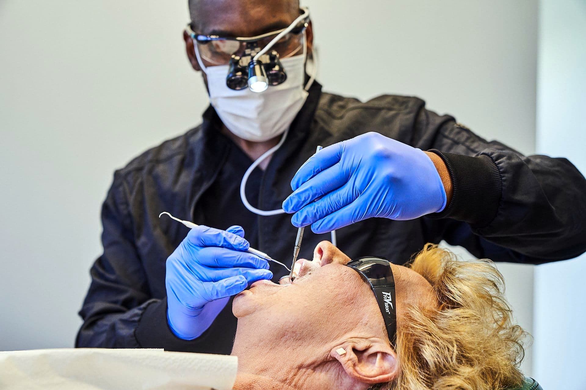 Dentist with magnifying glasses and mask working on a patient's teeth in a dental office.