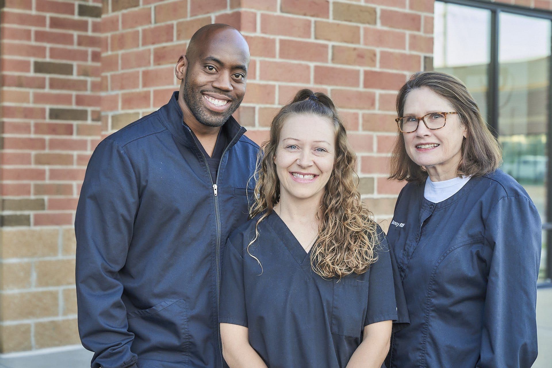A man and two women are posing for a picture in front of a brick building.