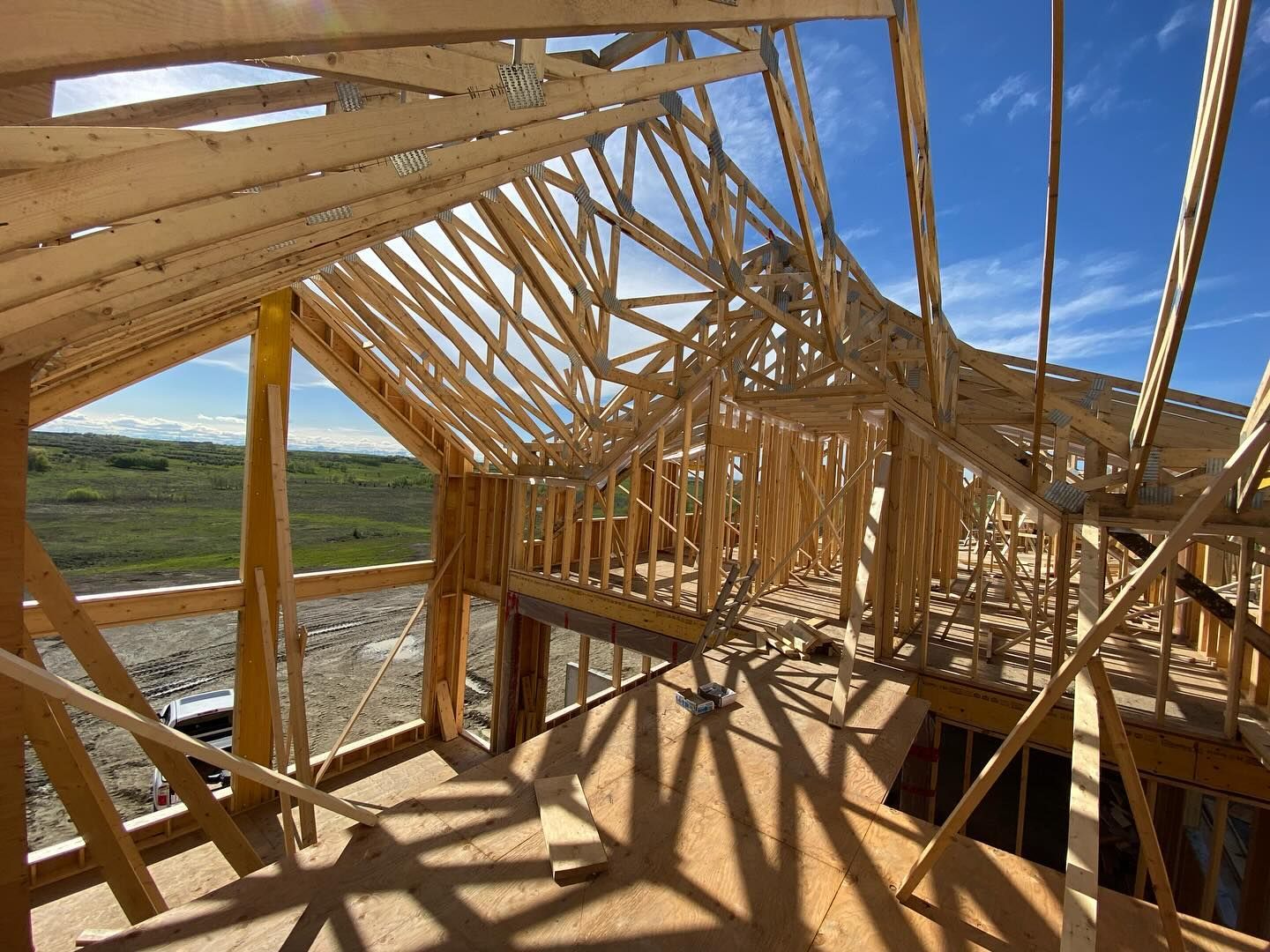 Wooden house framing under construction with exposed trusses and a blue sky overhead