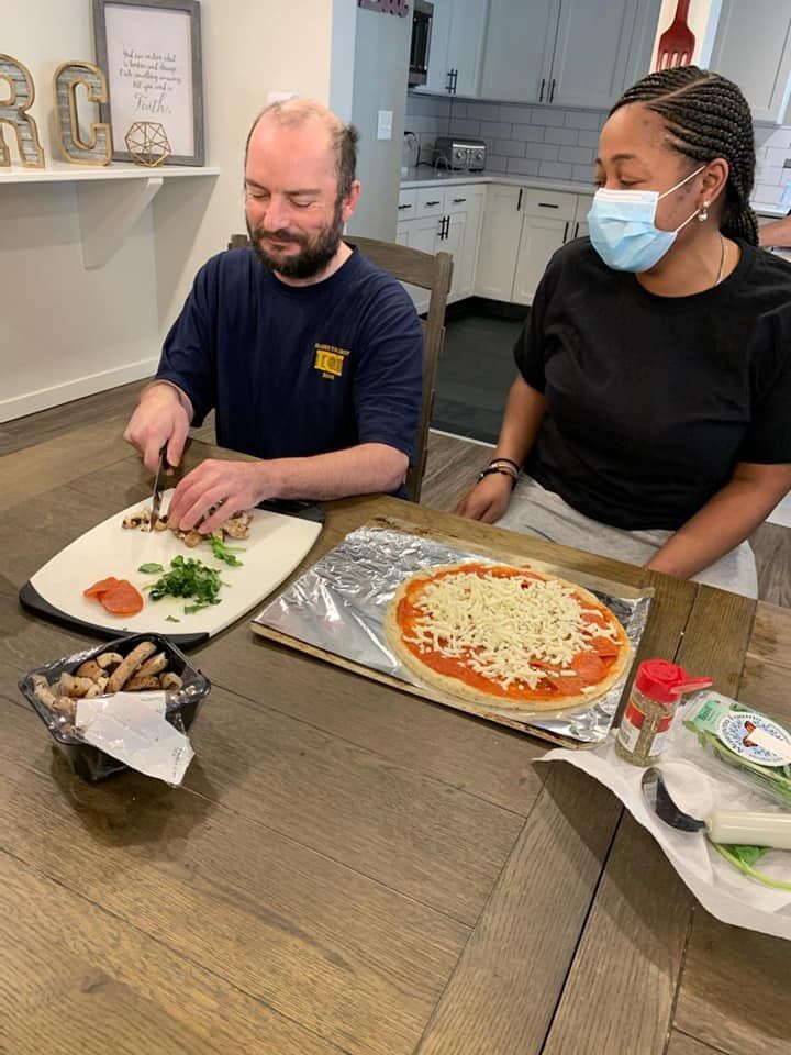 A man and a woman are sitting at a table making a pizza.