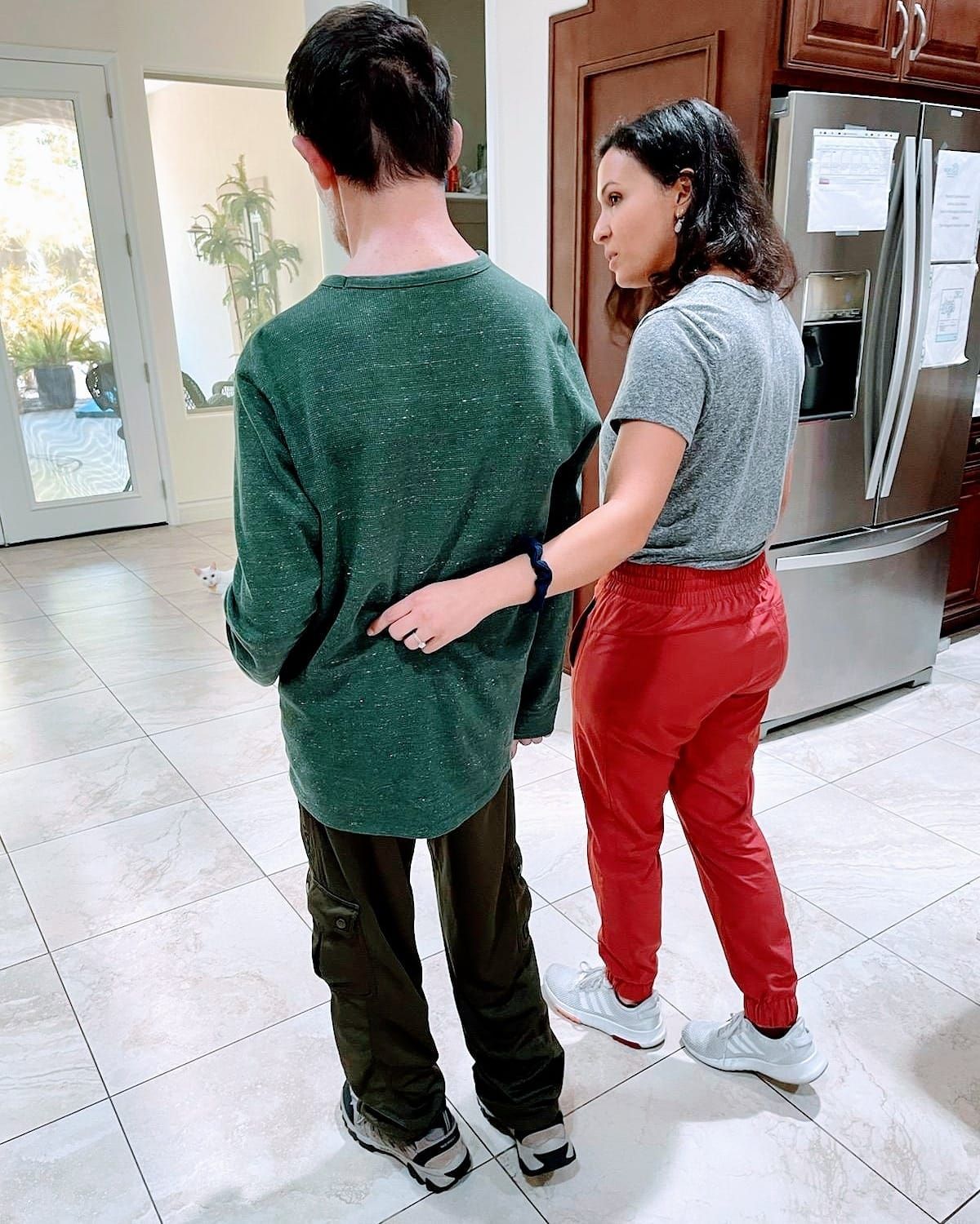 A woman is standing next to a boy in a kitchen.