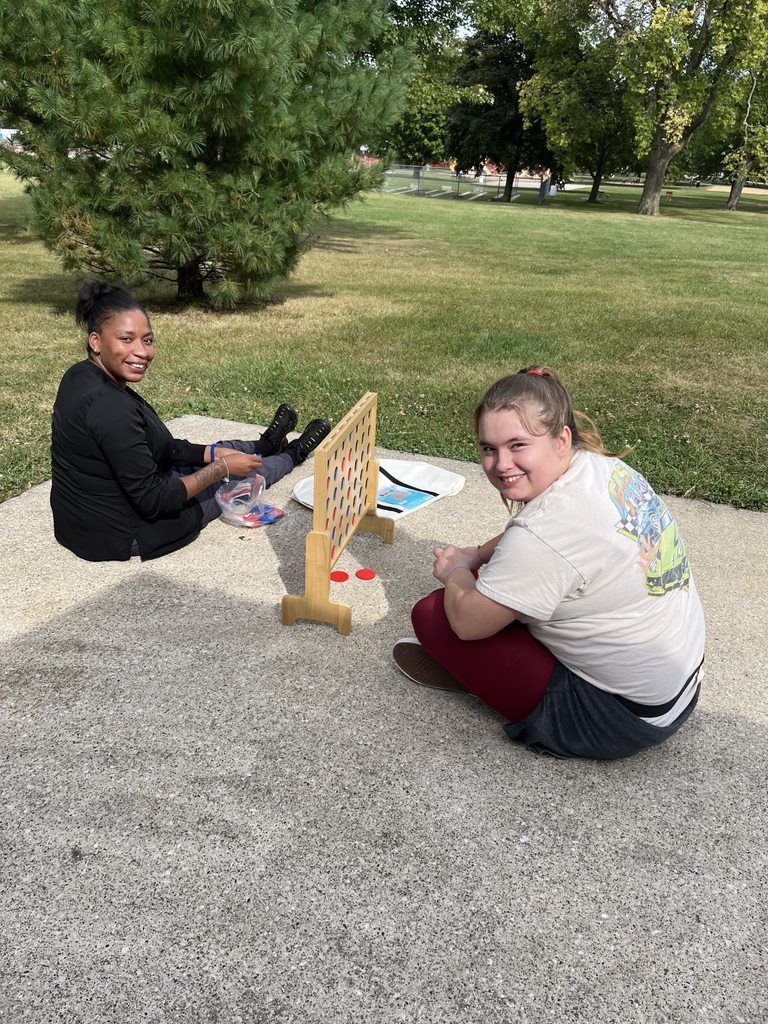 Two women are sitting on the ground playing a game in a park.