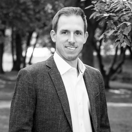 A man in a suit and white shirt is smiling in a black and white photo.