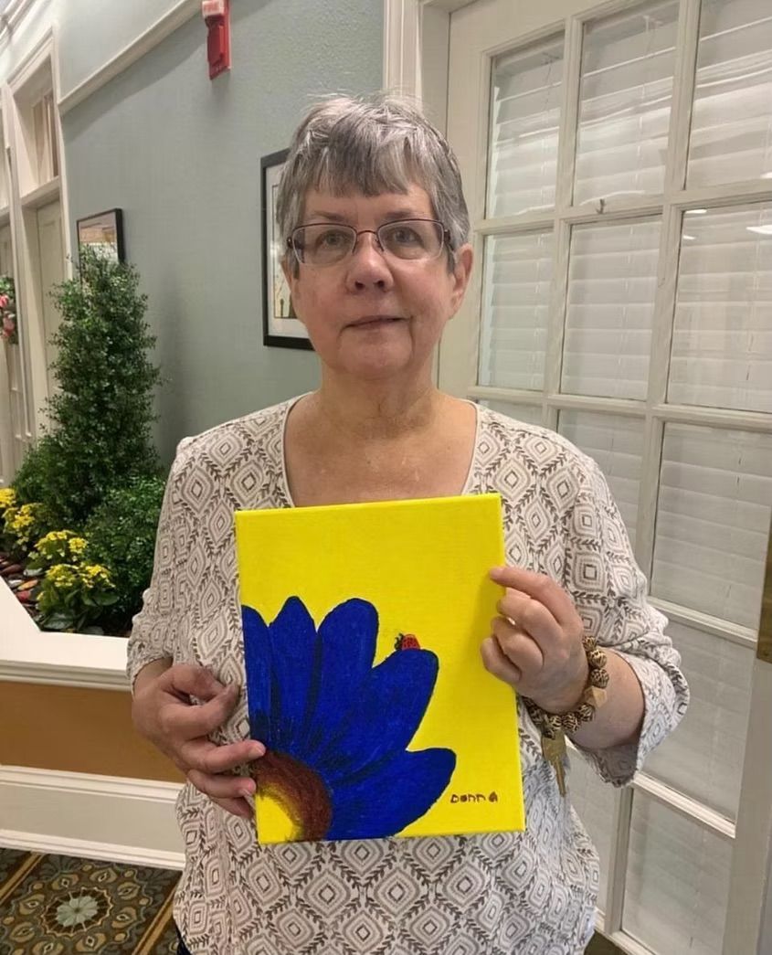 A woman is holding a painting of a blue flower on a yellow background.
