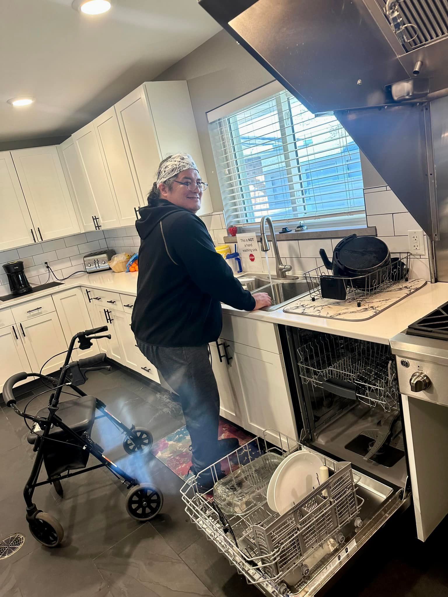 A woman in a wheelchair is standing in a kitchen loading a dishwasher.