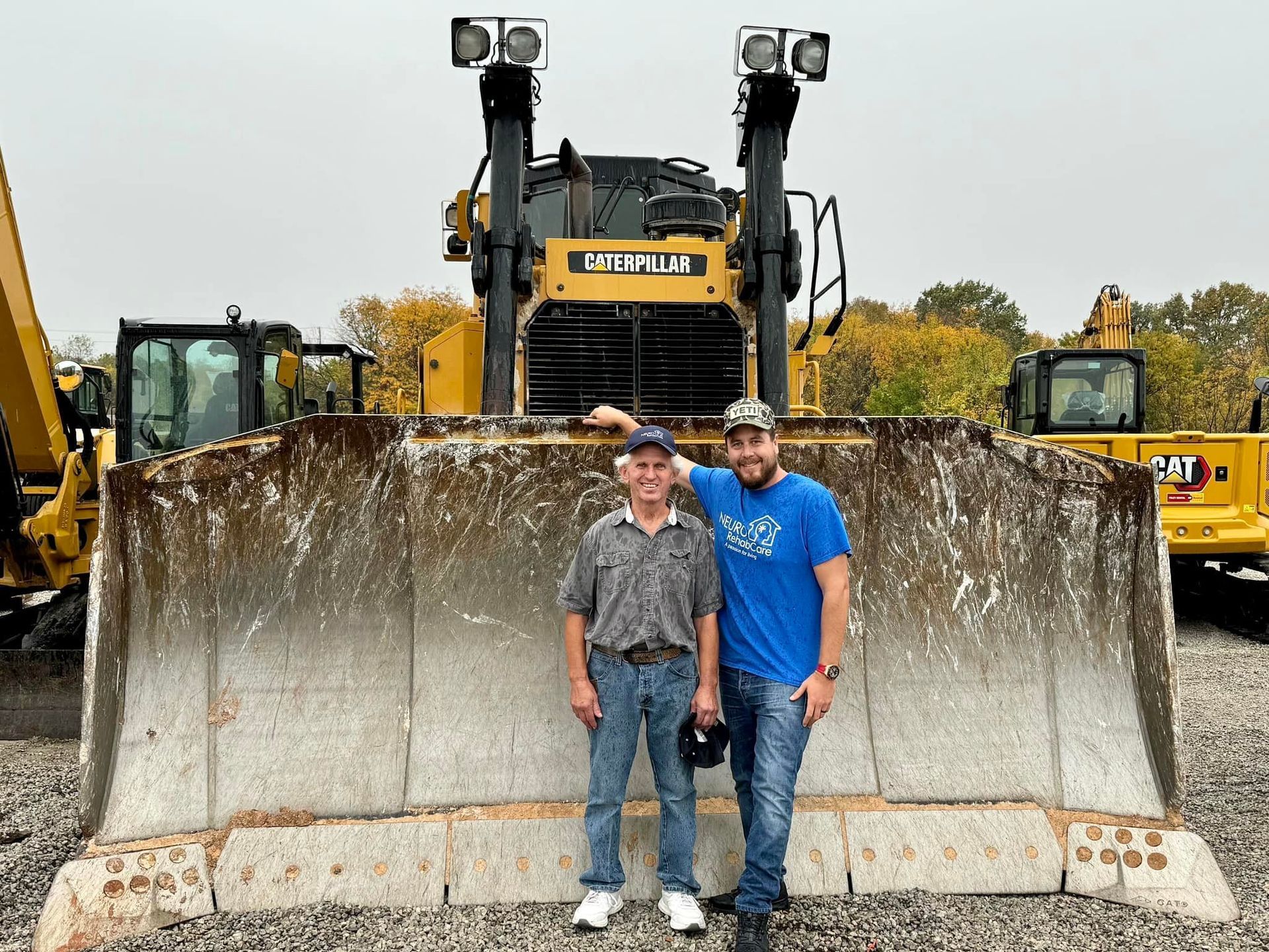 Two men are standing in front of a bulldozer.