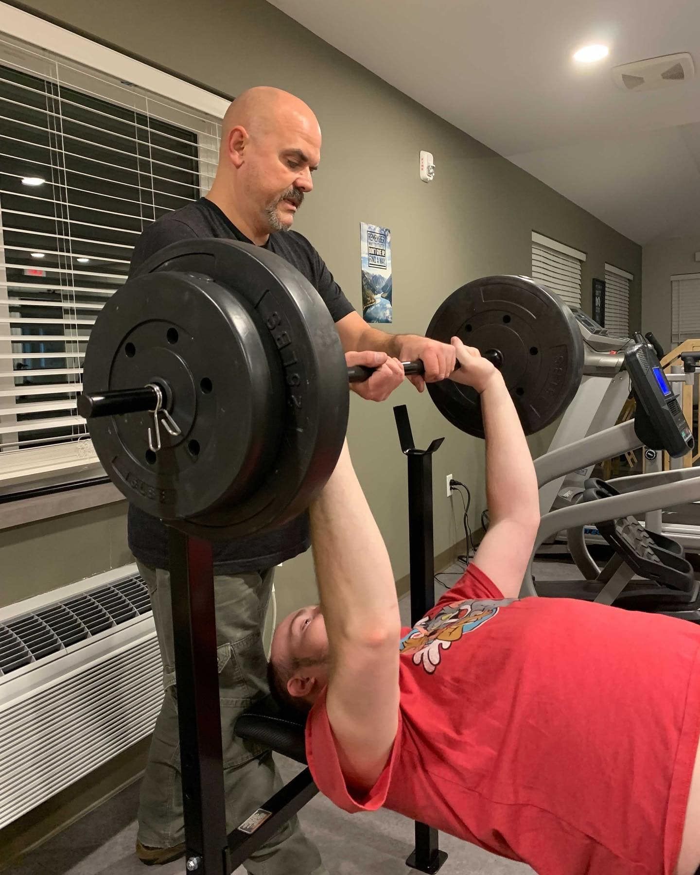 A man is helping a man lift a barbell on a bench in a gym.