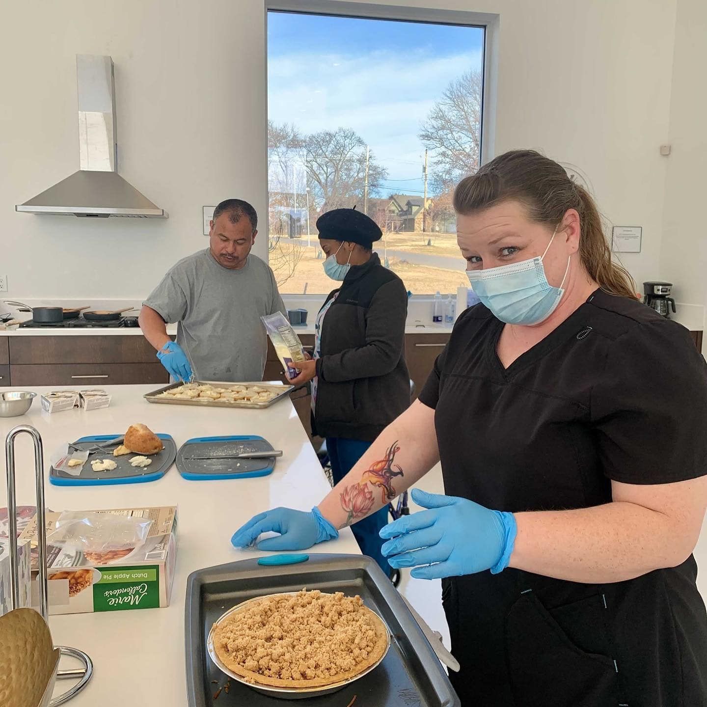 A woman wearing a mask is preparing a pie in a kitchen