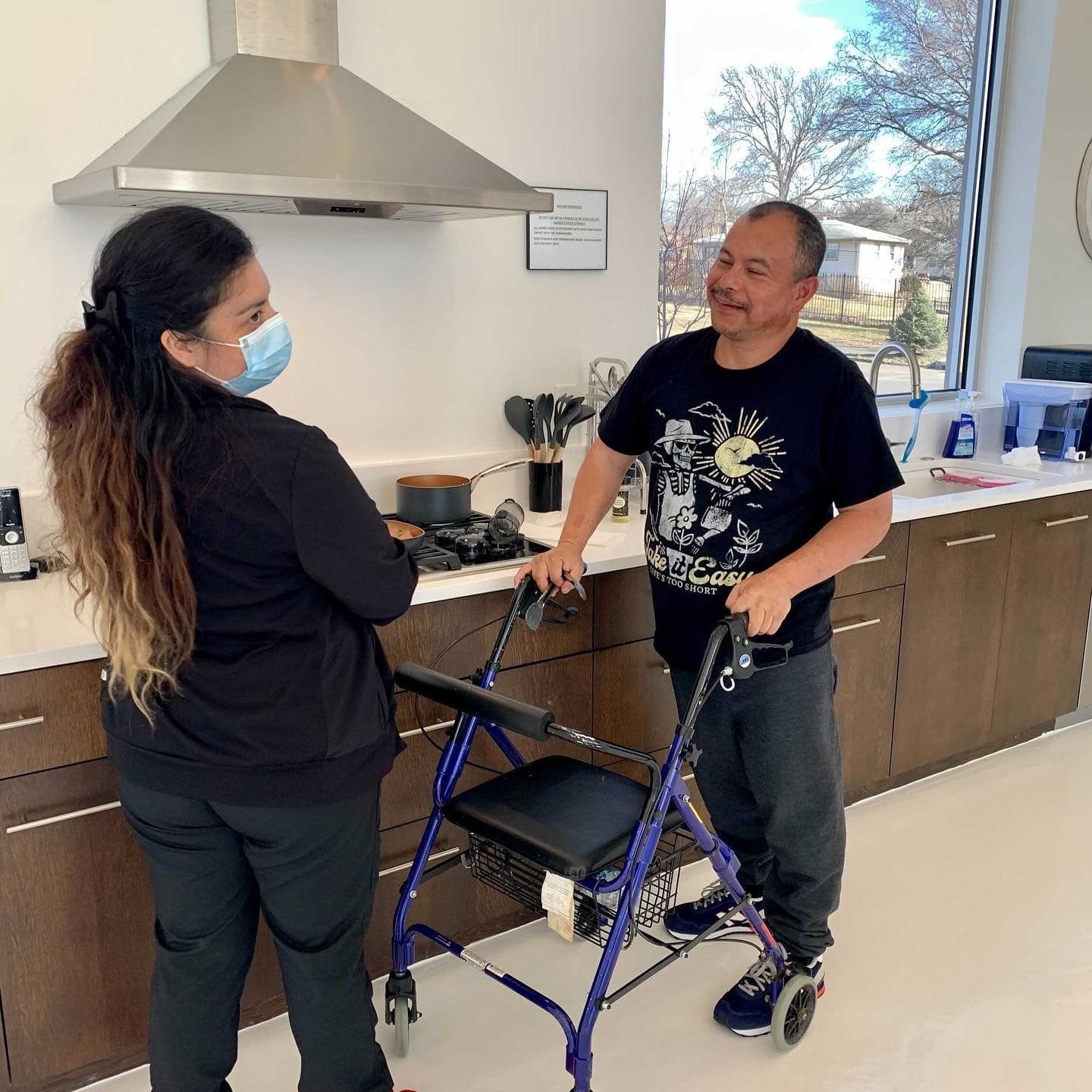 A man with a walker is talking to a woman in a kitchen