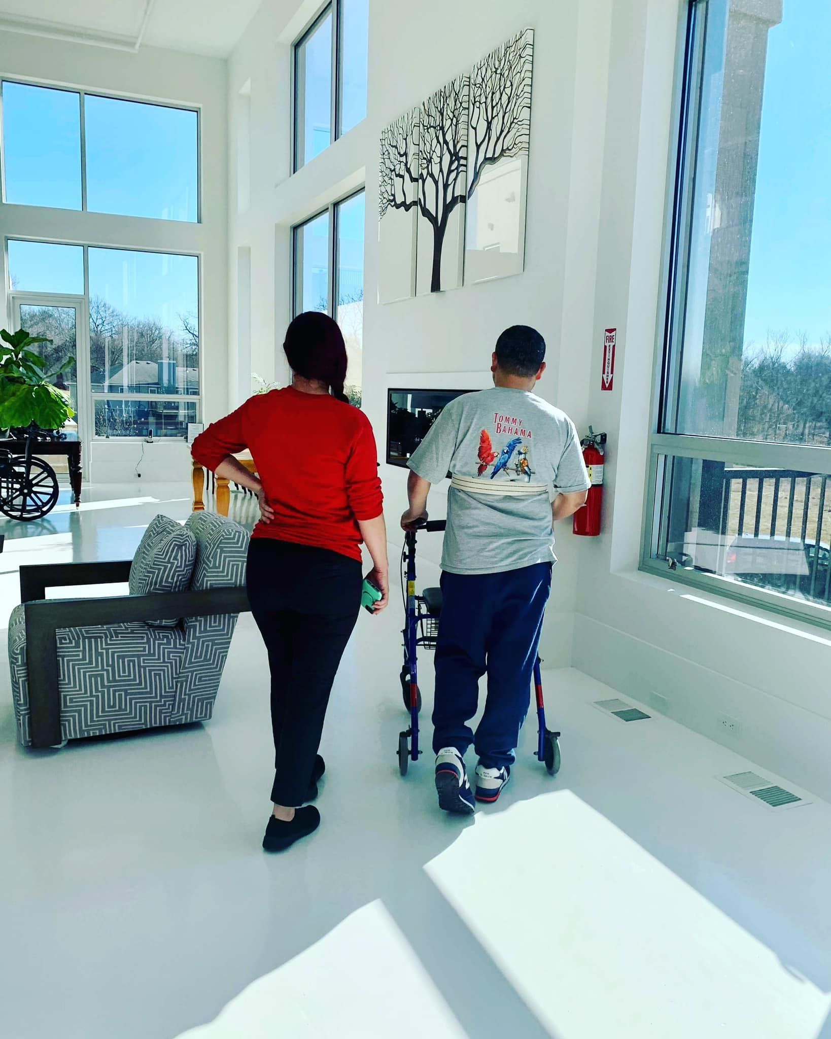 A man with a walker is walking next to a woman in a living room.