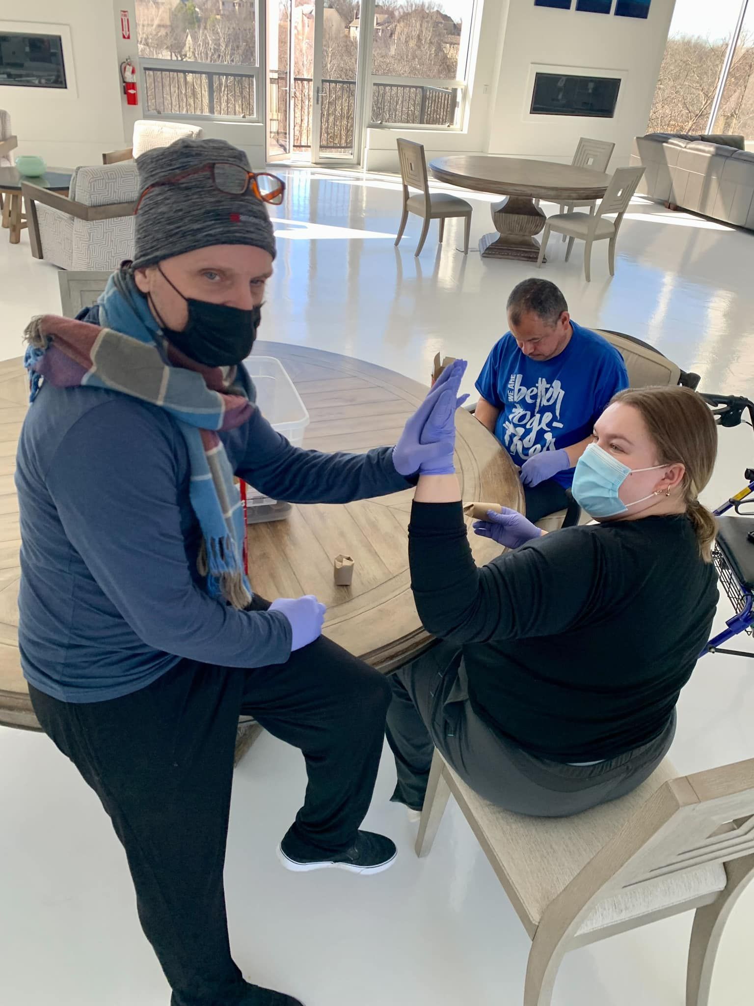 A man and a woman wearing masks and gloves are sitting at a table.