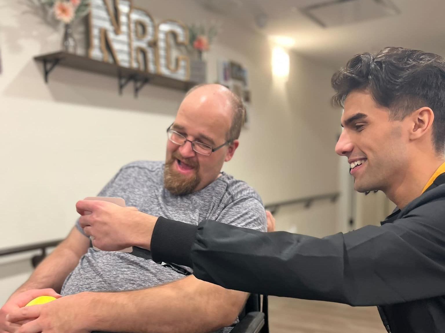 A man in a wheelchair is being helped by a young man.