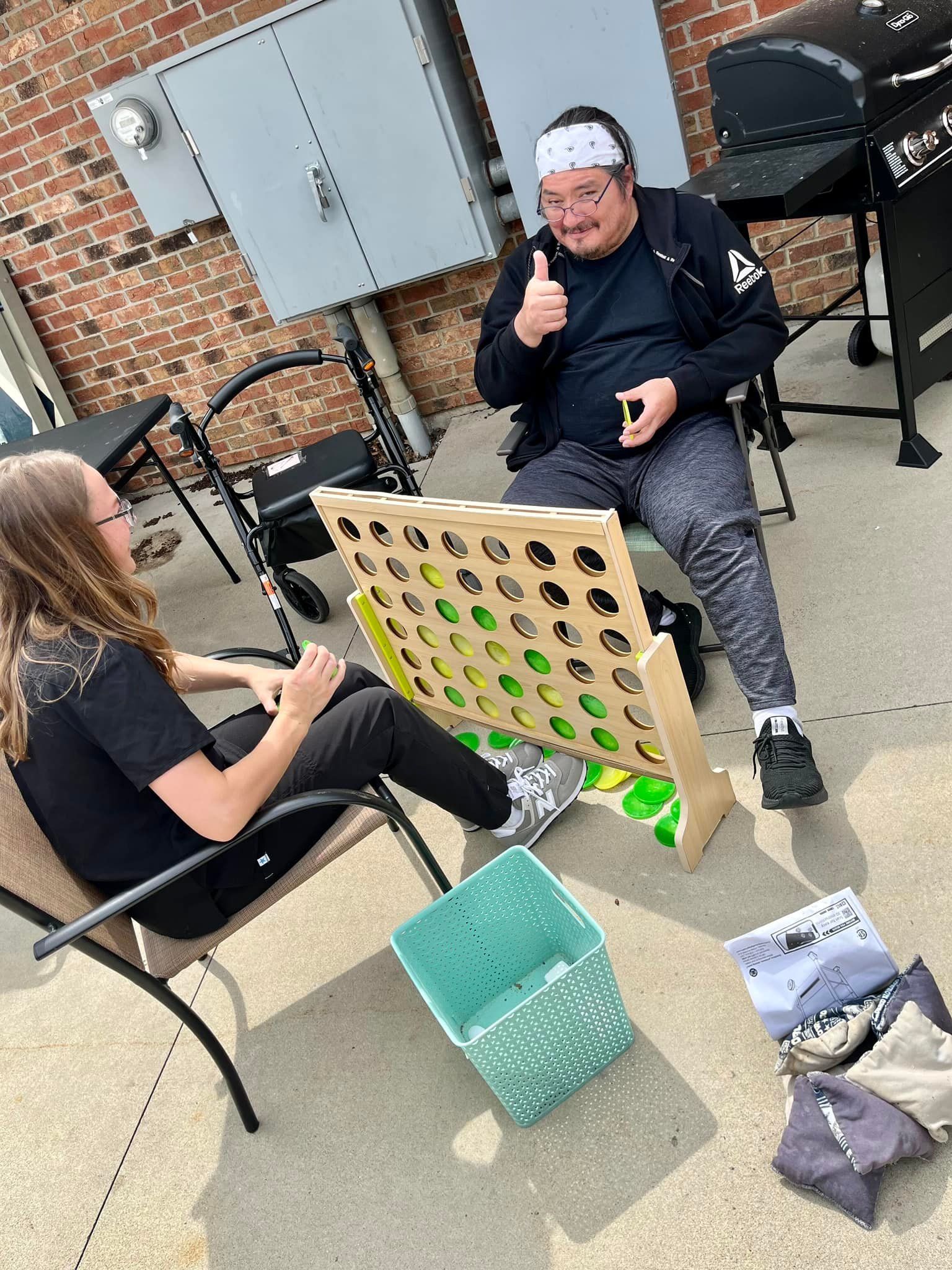 A man and a woman are playing connect four on a patio.